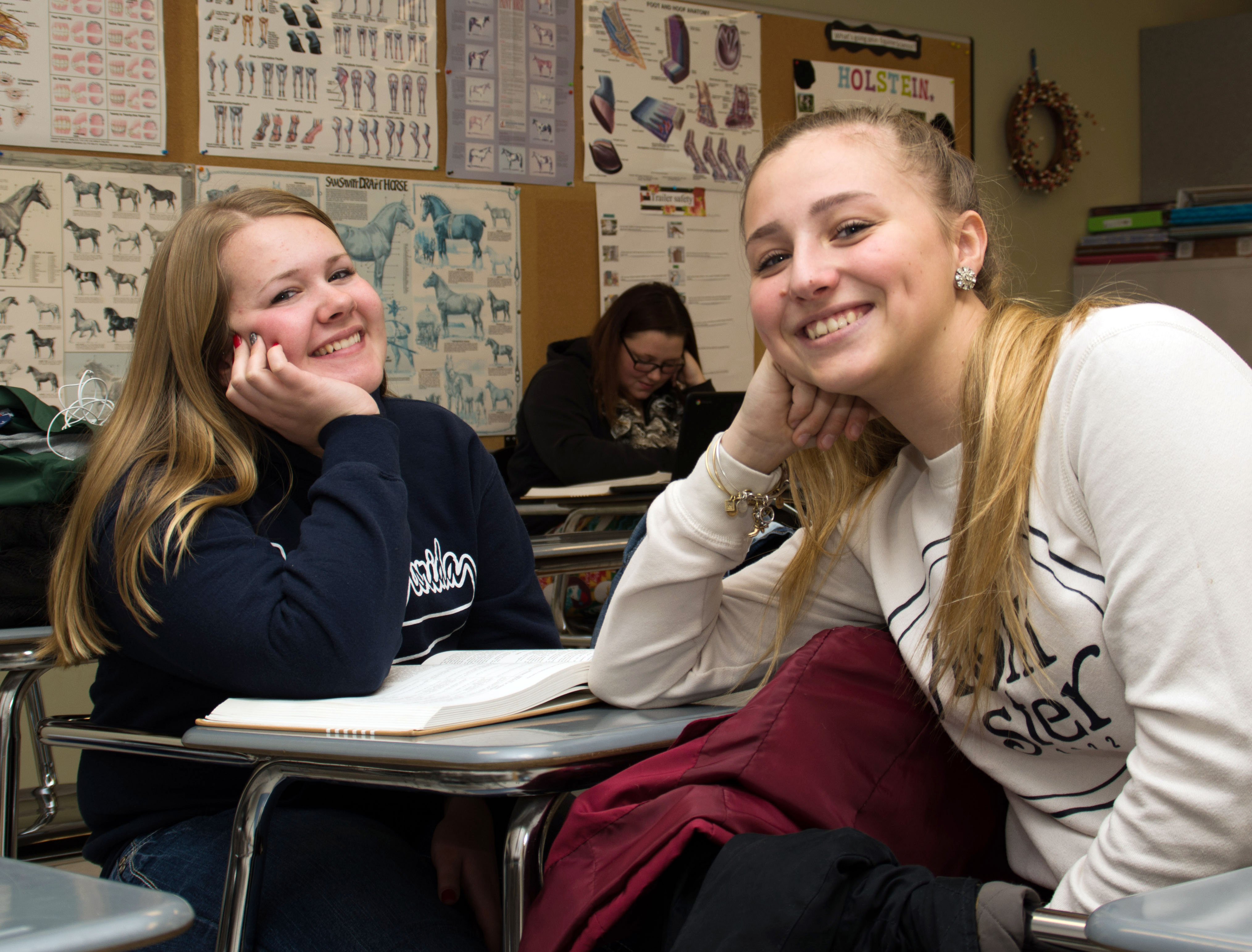 students students sit at desk and smile at the camera