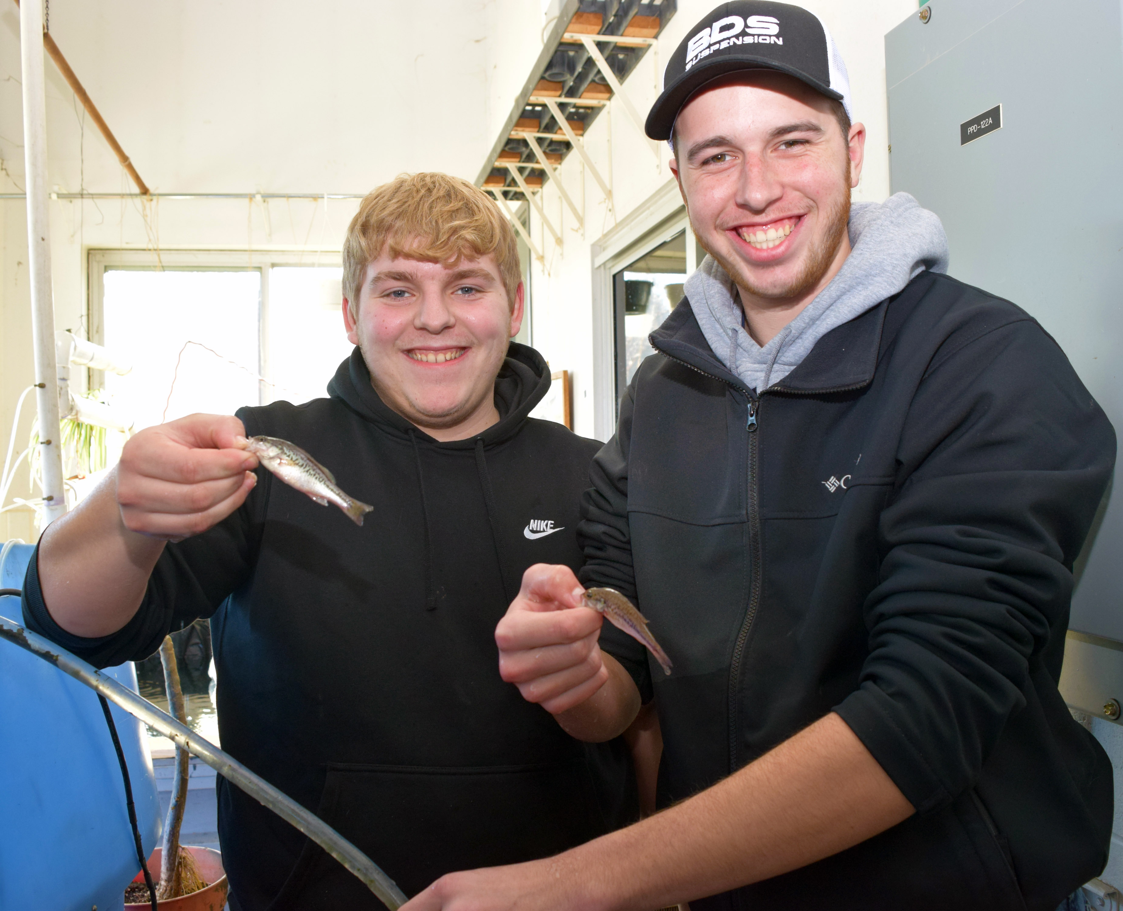 Two students smile for the camera each holding one small fish.