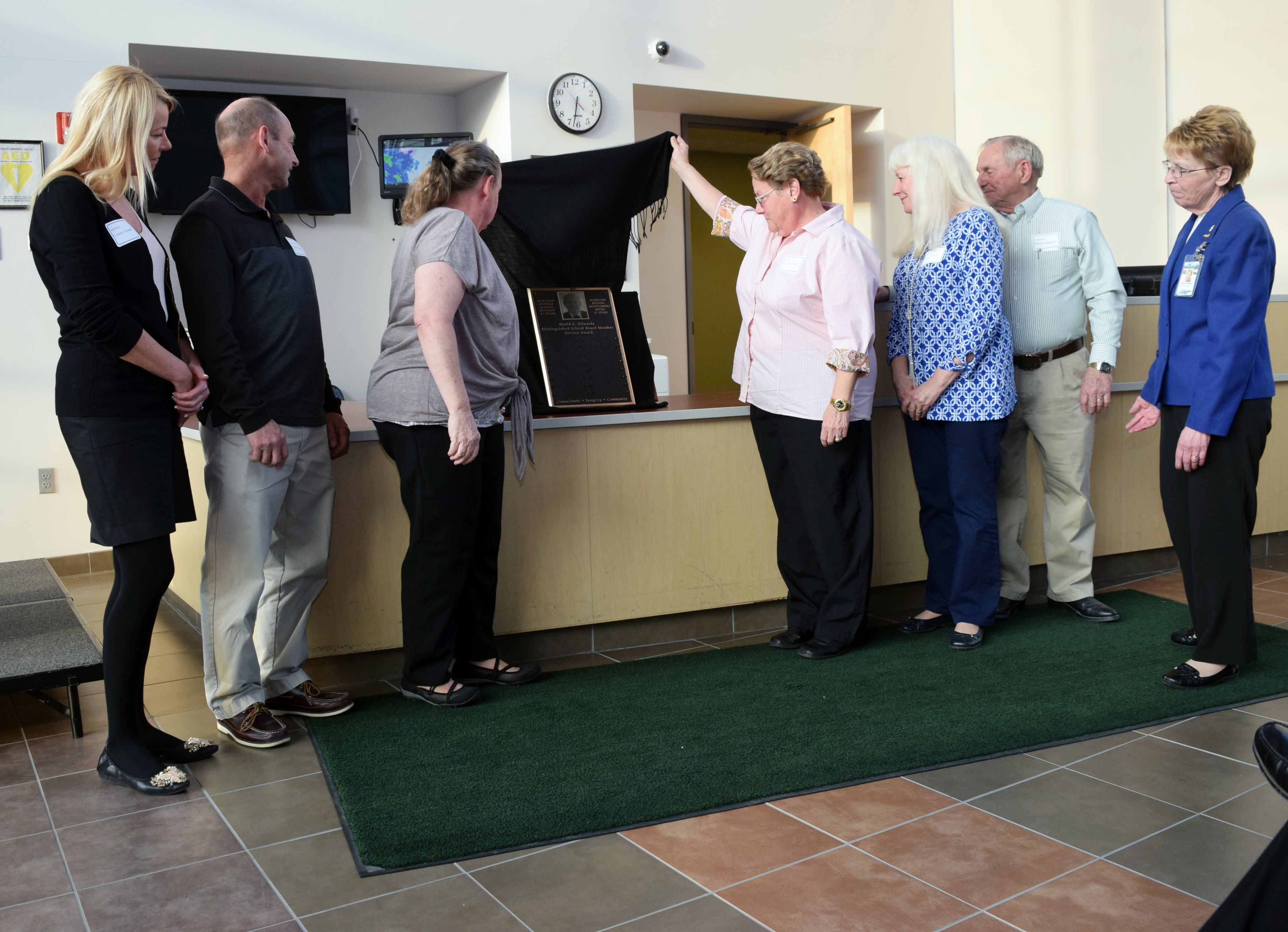 Two woman remove a black cloak from a bronze plaque as others look on. 