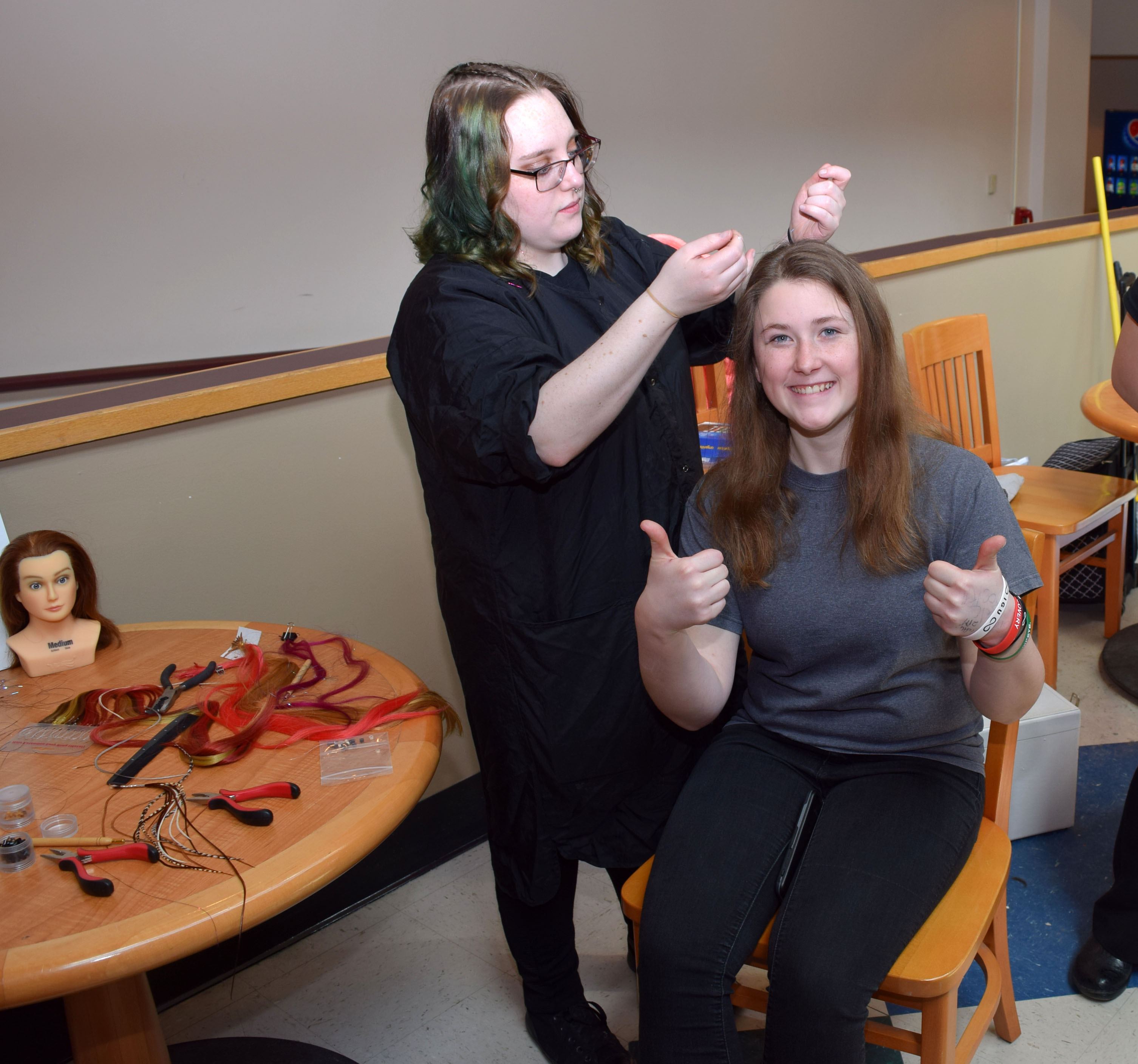 A student cosmetologist puts in glitter strands in another students hair 