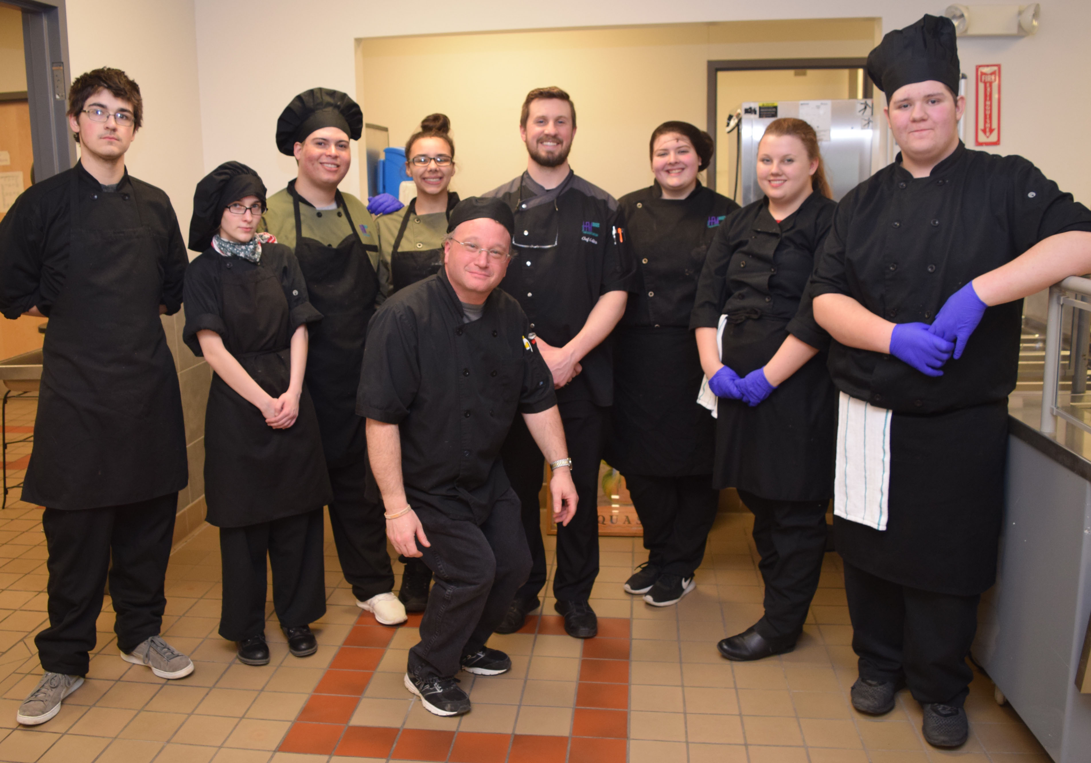 Students and instructors in culinary outfits pose for a photo.