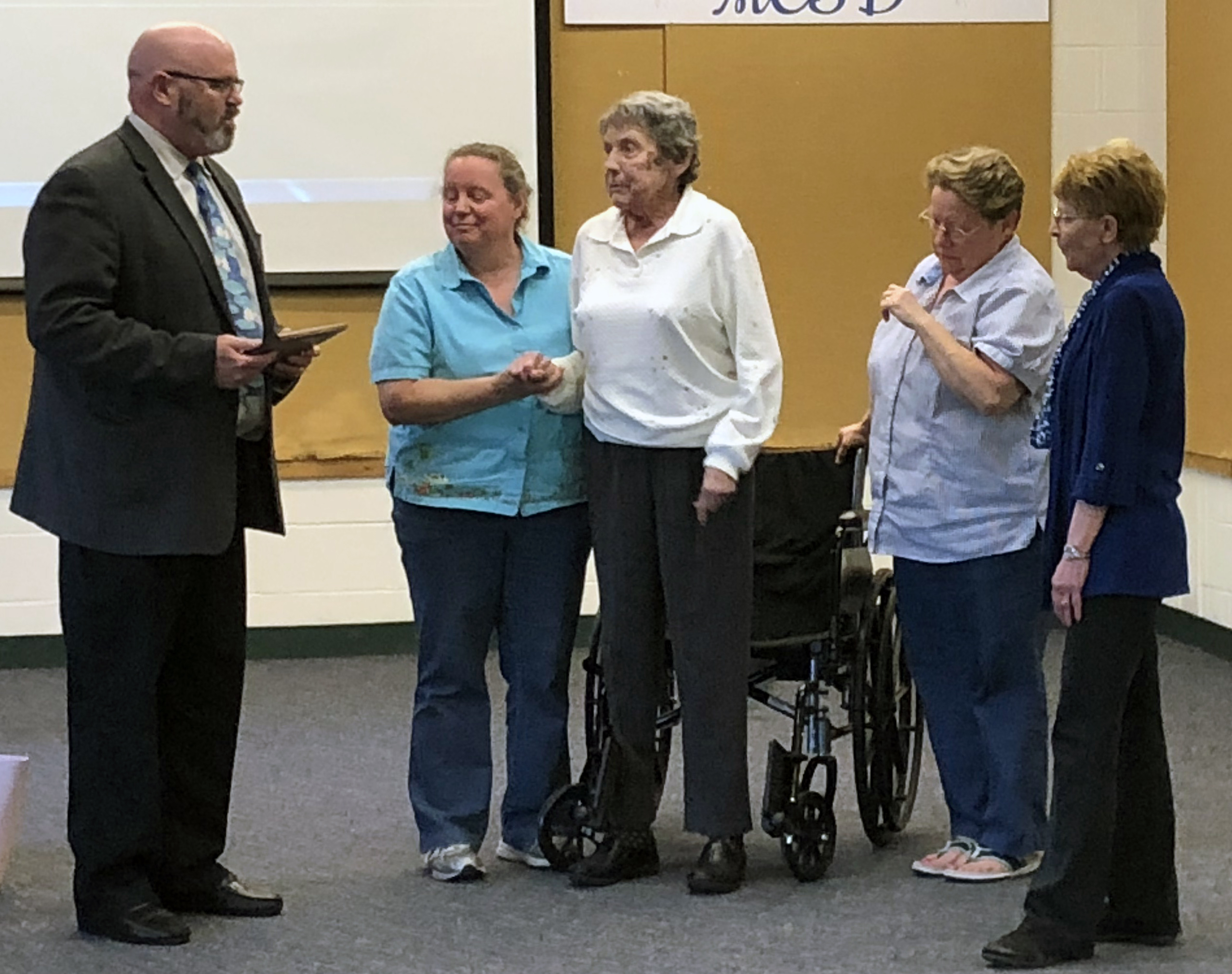 Dr. Michel holds a plaque in his hands speaking with Mr. Edwards' daughters, wife and Joanne Freeman to his left.