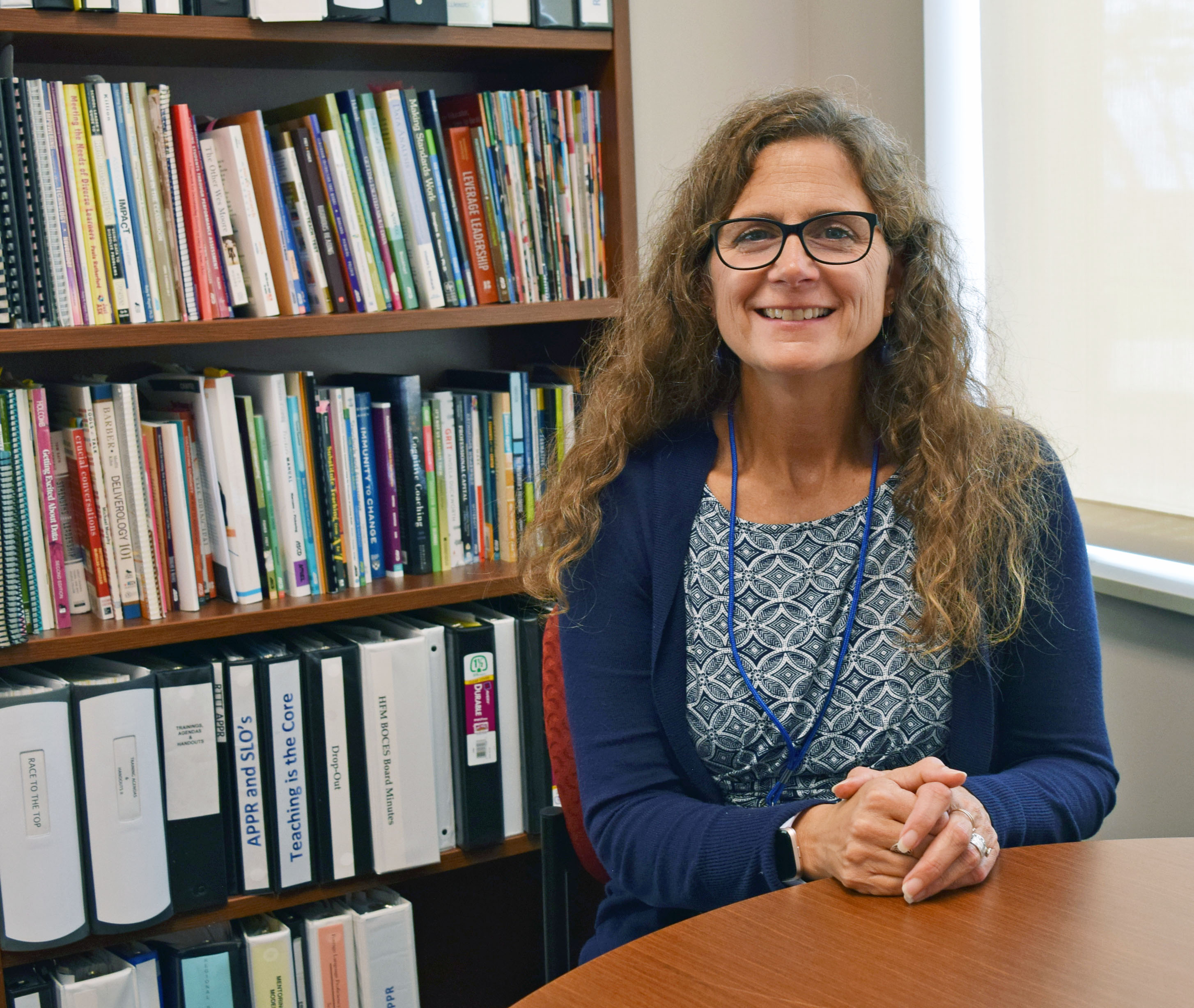 Tara Caraco sits at a desk with a bookshelf filled with books behind her