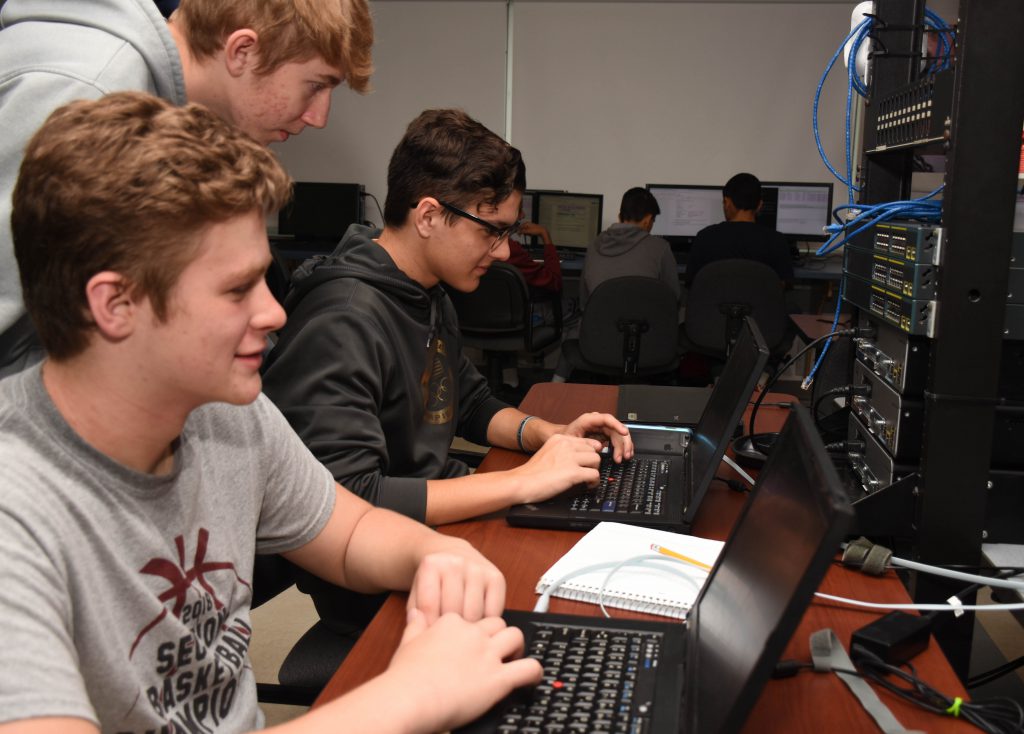 three students work at laptop with wire and computer cables in the background.