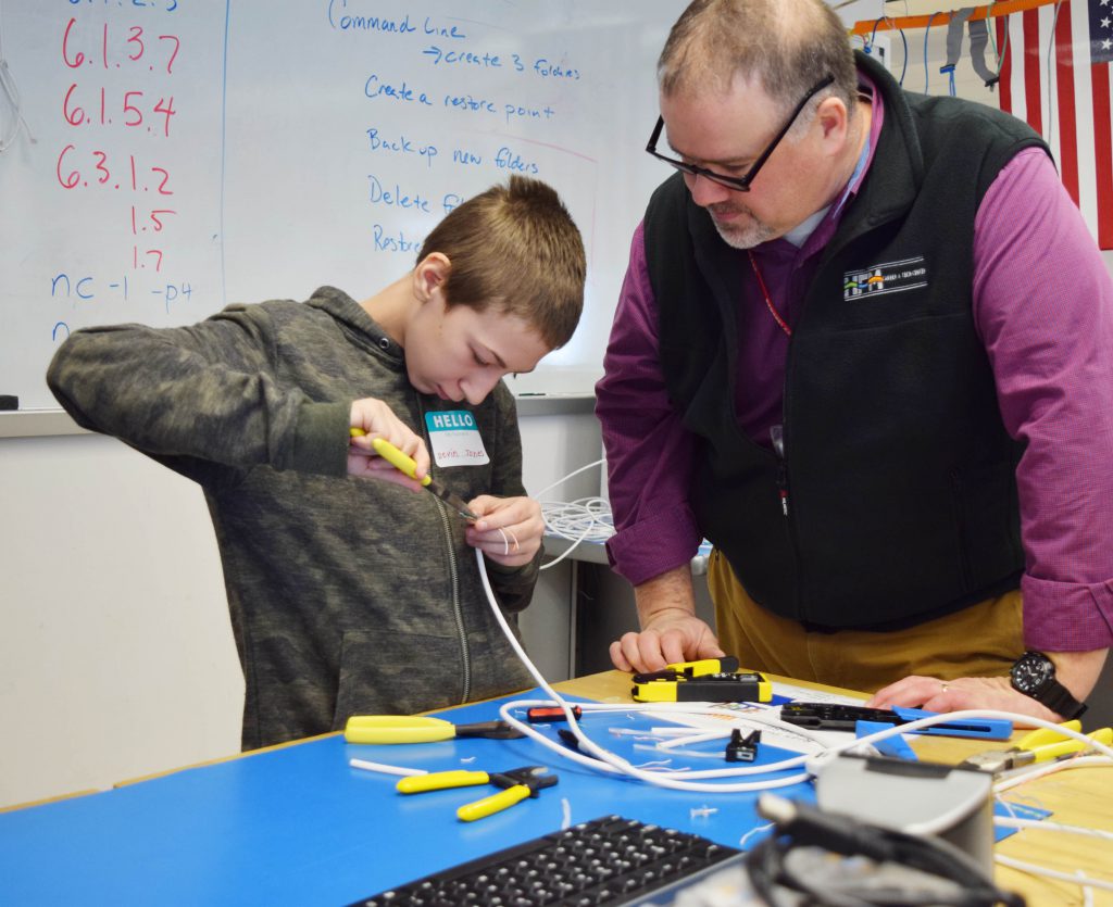 A student uses a needle nose pliers to terminate a cable as Mr. Mahon looks on. 