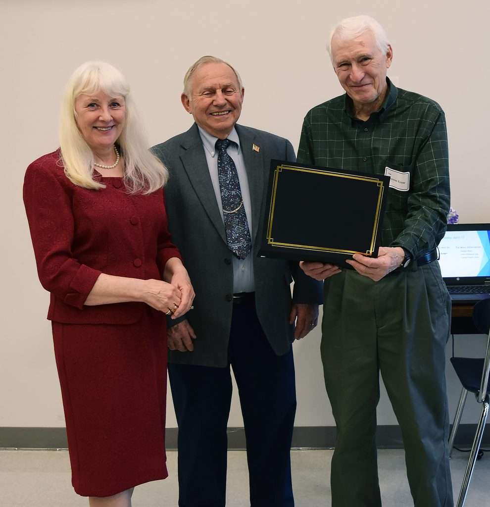 Three people stand in a row with Reese at right holding a certificate.