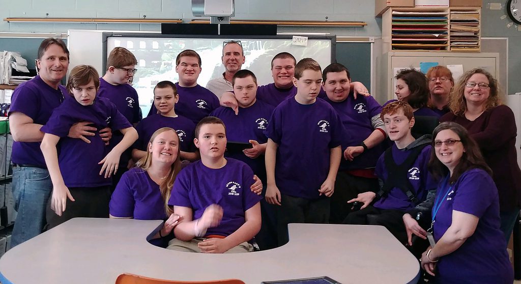 Dellis, in the background, poses with a large group of students and staff.