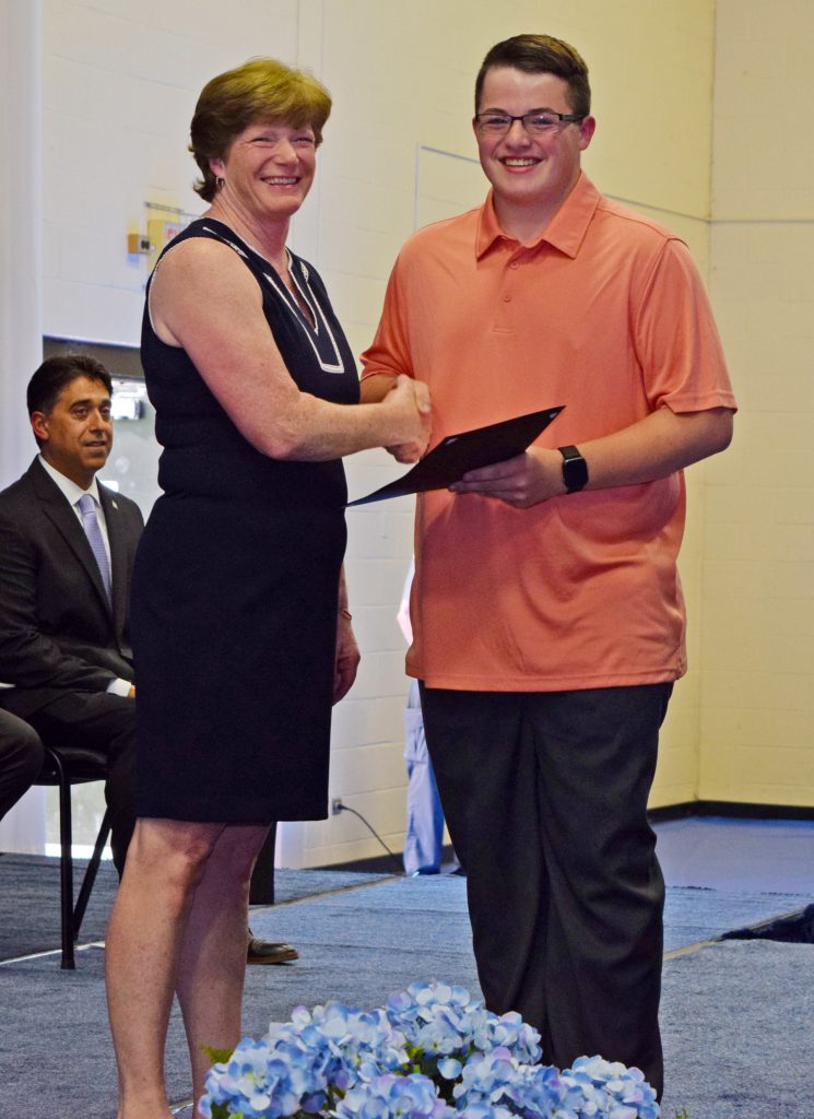 A teacher hands a students a certificate while shaking hands.