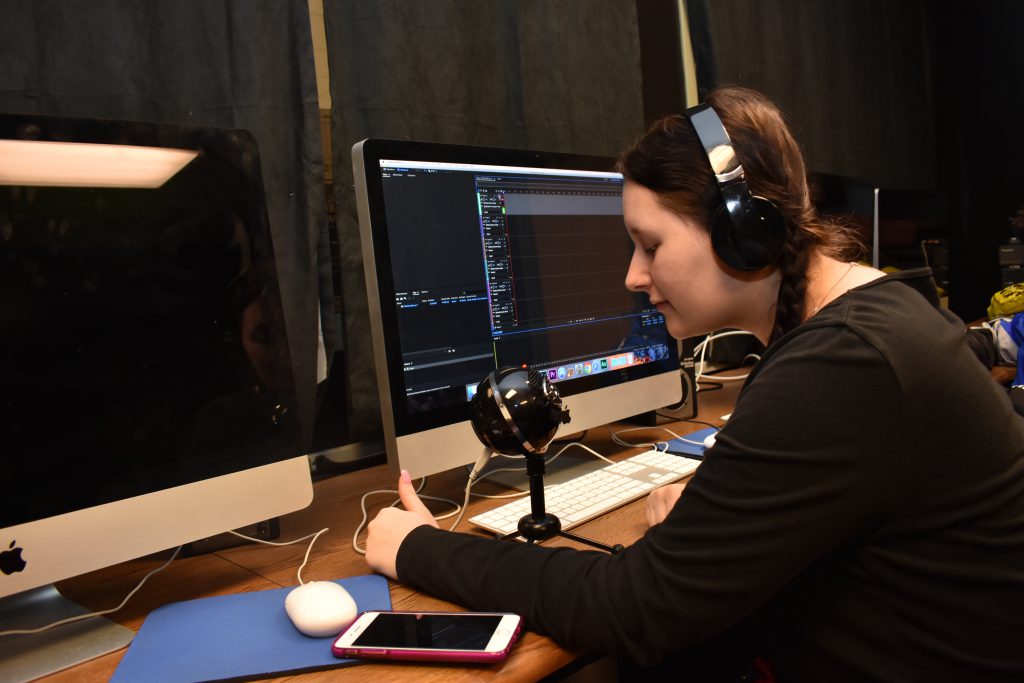 A student wears headphones and speaks into a recording device