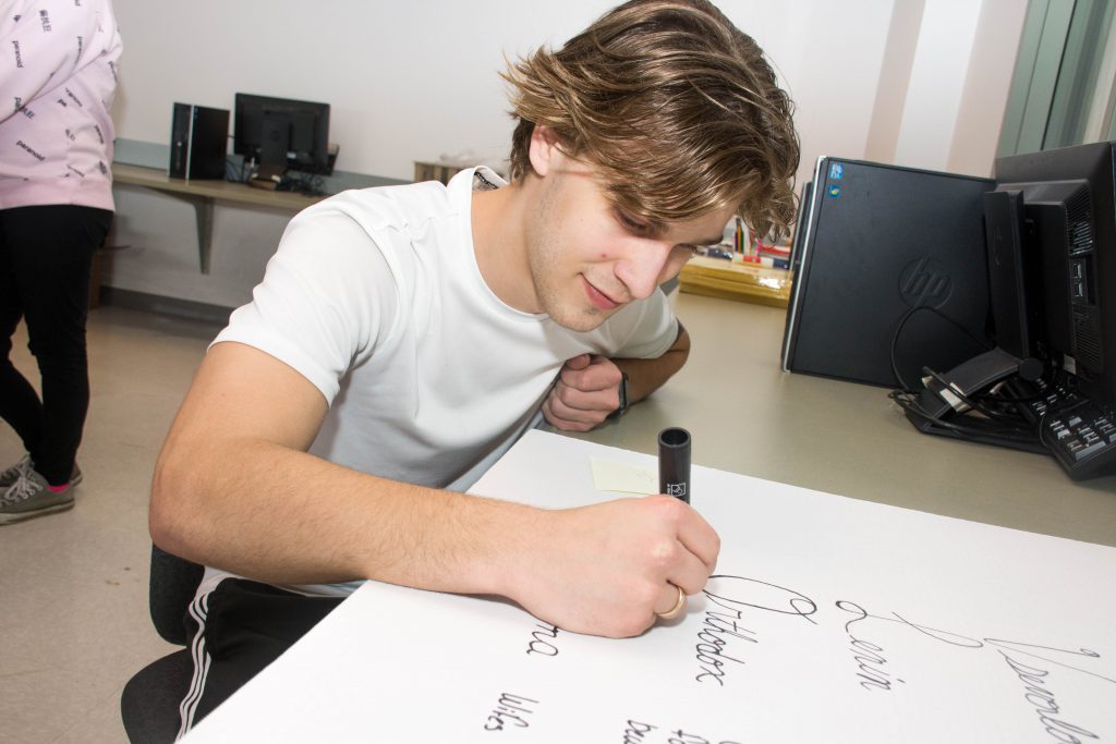 A student sits at a desk and uses a marker on poster board.