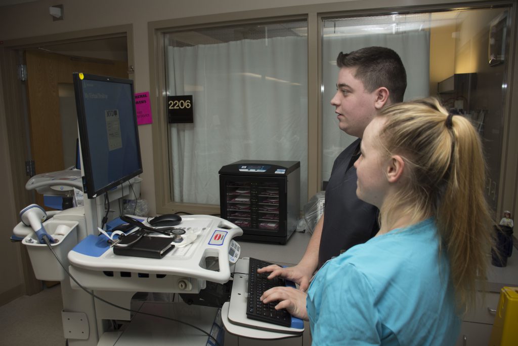 Two student work on a portable medical station in a hospital hallway