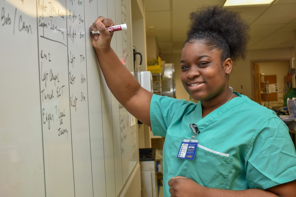 A student in scrubs writes on a dry erase board