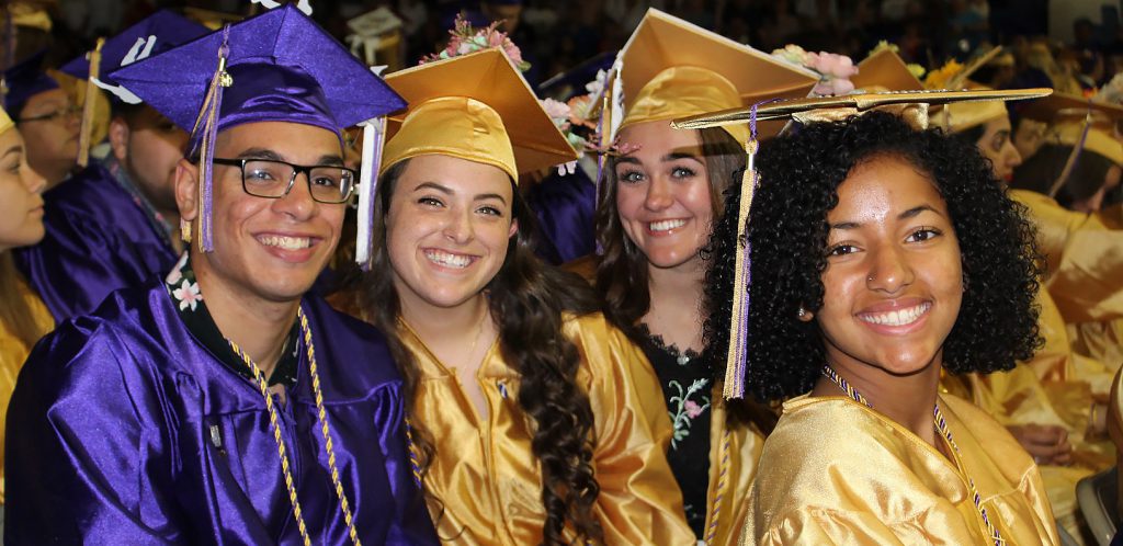 four graduates in caps and gowns smile at the camera
