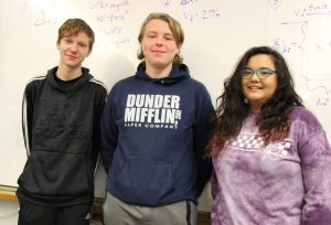 three students posing in front of a whiteboard