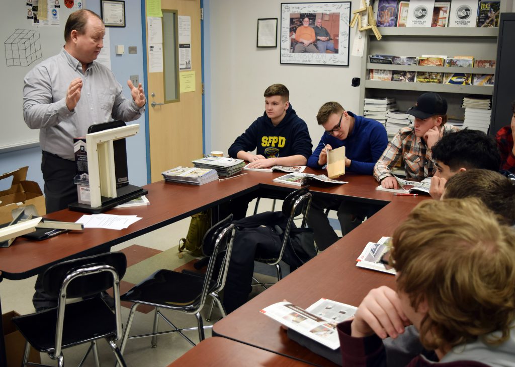 Scott Dewsbury of Reeb Millwork refers to a door cut out as students sit at tables listening.