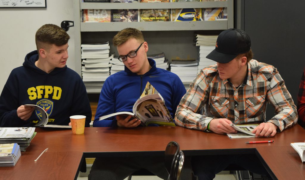 Three students look over Reeb Millwork catalogs.