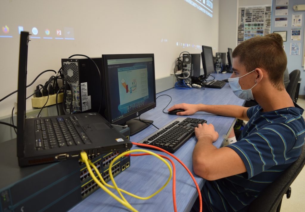 A student sits at a computer and a laptop