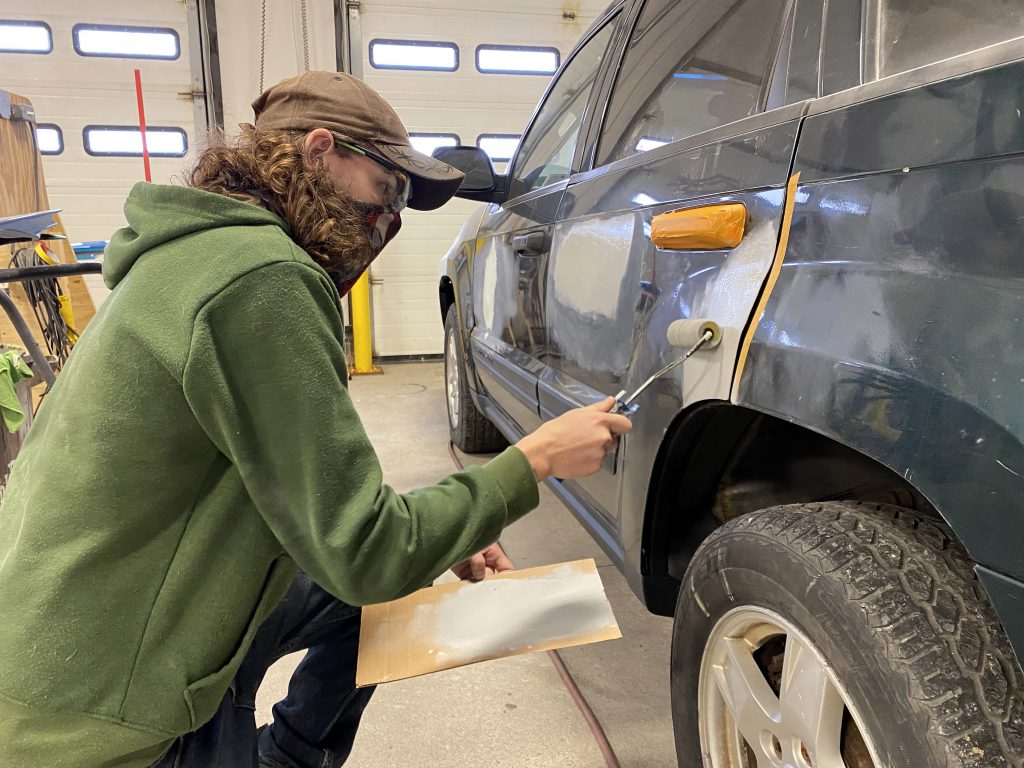 A student applies auto body primer to a vehicle with a roller