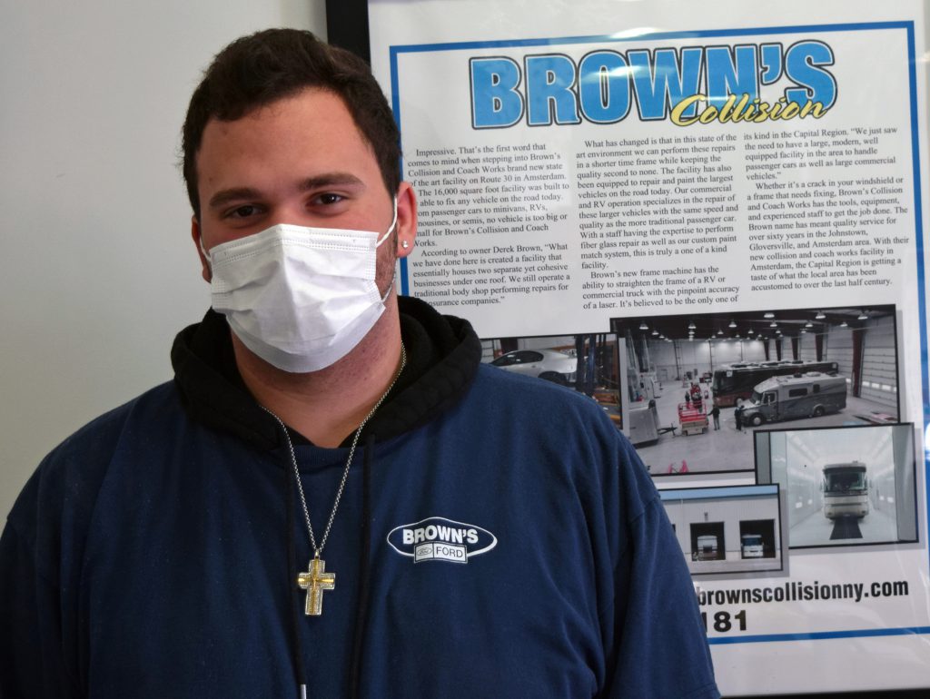 Anthony Darpino poses for a photo next to a Brown's Collision poster hanging on a wall