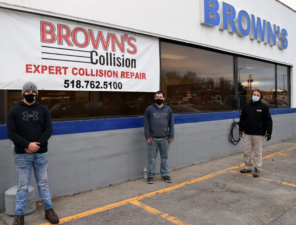 Three people stand outside of Brown's Ford in Johnstown posing for a photo,