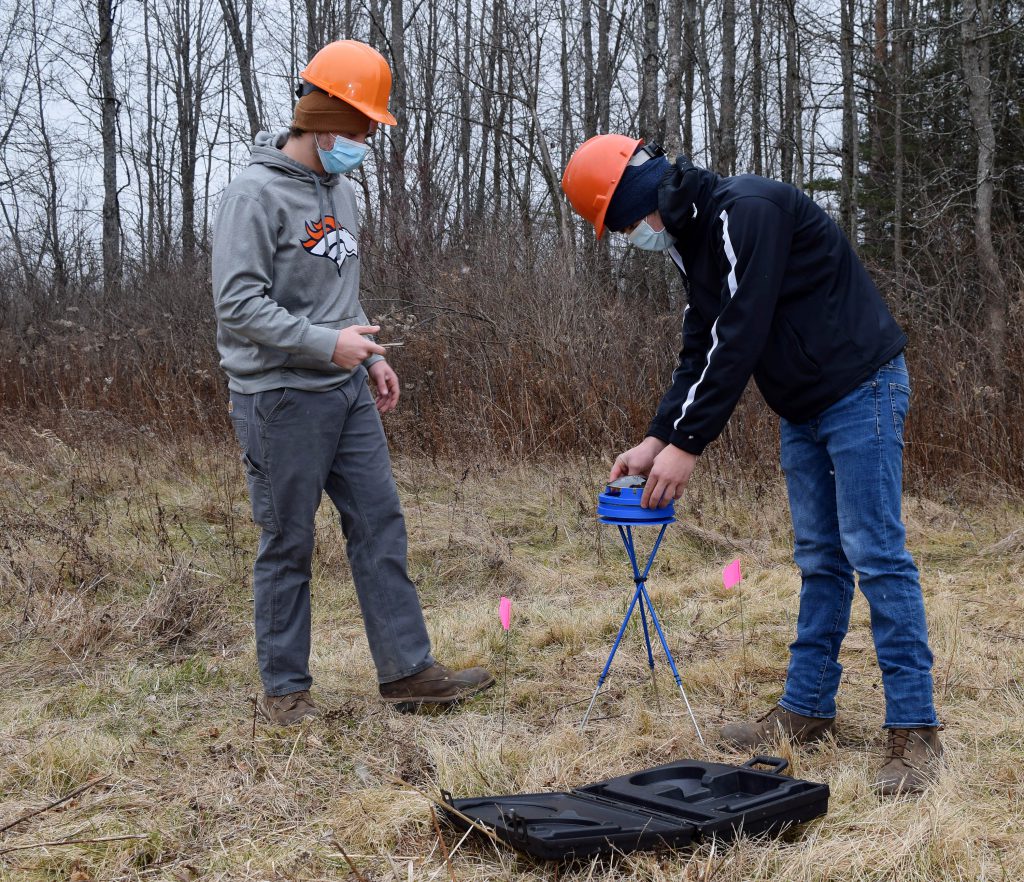 Two students adjust a Solar Pathfinder in a field.