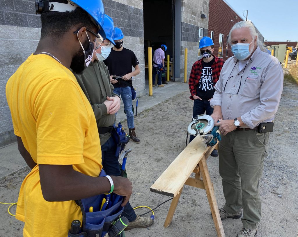 An instructors show a circular saw as three students look on.