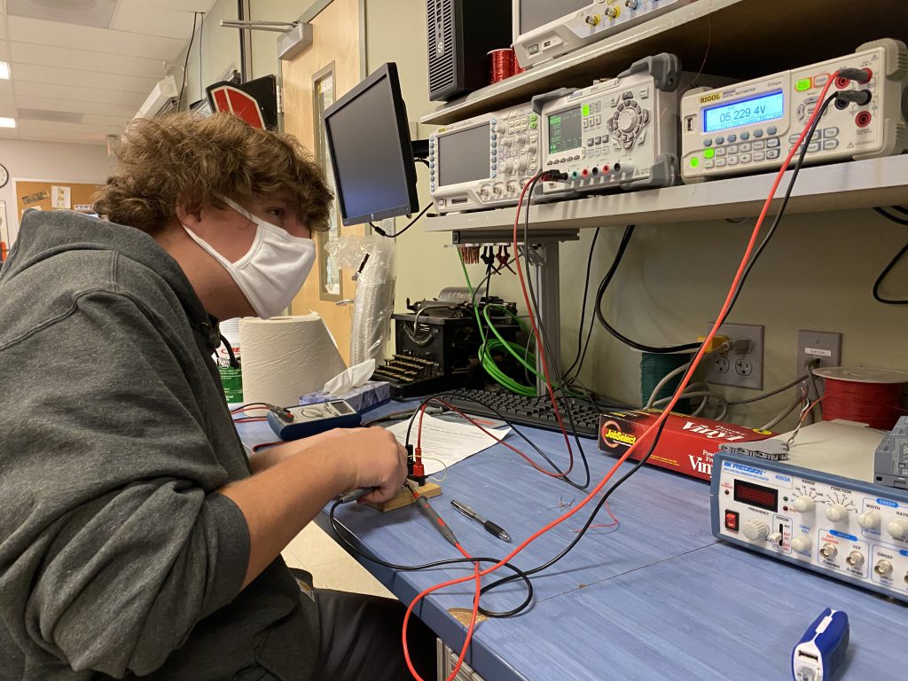 A student uses a desktop meter to measure electrical components while sitting at a desk. 