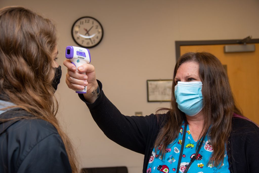 Nurse Kim Bursese uses a digital point and shoot thermometer to check a student's temperature