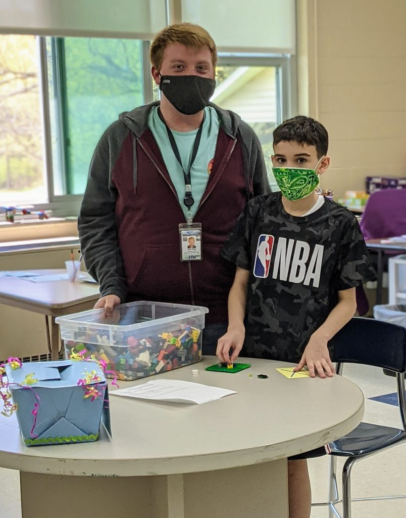 An adult and a student stand by a table with Legos on it