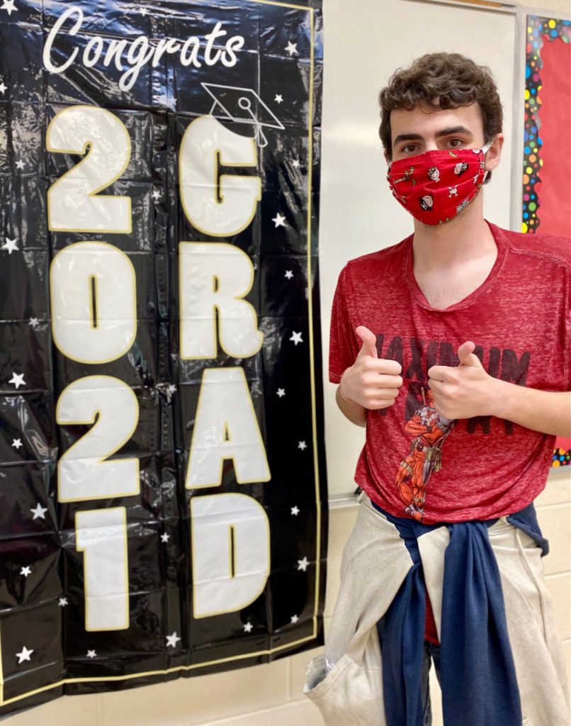 Sean gives the thumbs up standing next to a 2021 graduation banner