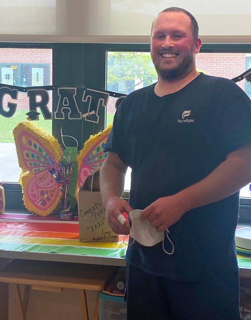 photo of Tyler smiling for a photo in front of a graduation banner and a large paper butterfly