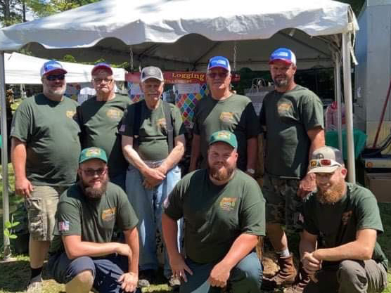 eight people wearing matching green t-shirts stand and kneel in two rows posing for a photo