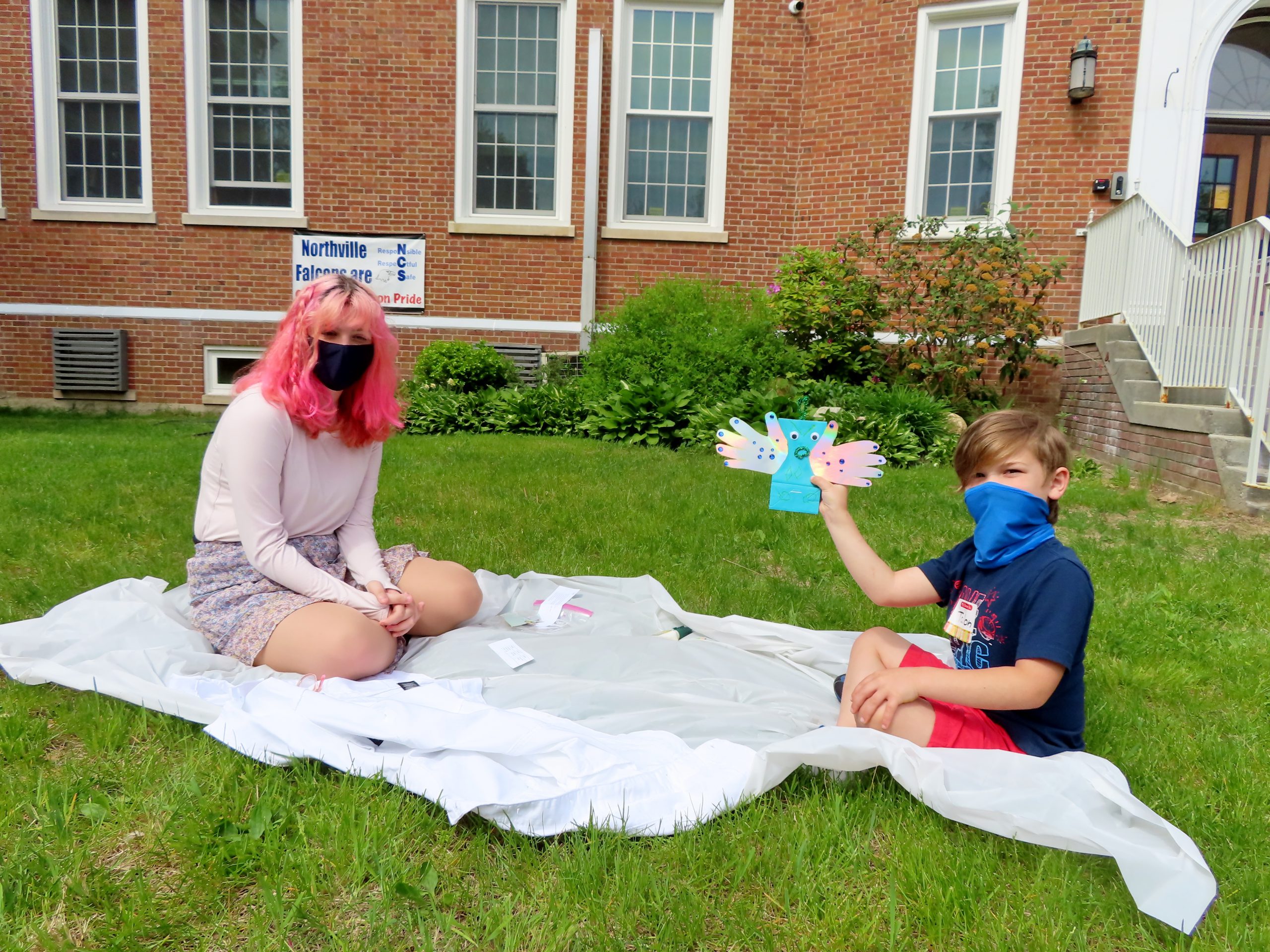 Two students sit on a blanket outside of the school