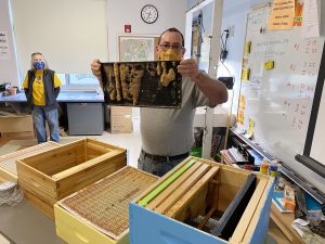 Jeff Fagan holds up a frame with honey combs on it as Kathryn Gulick looks on from the background