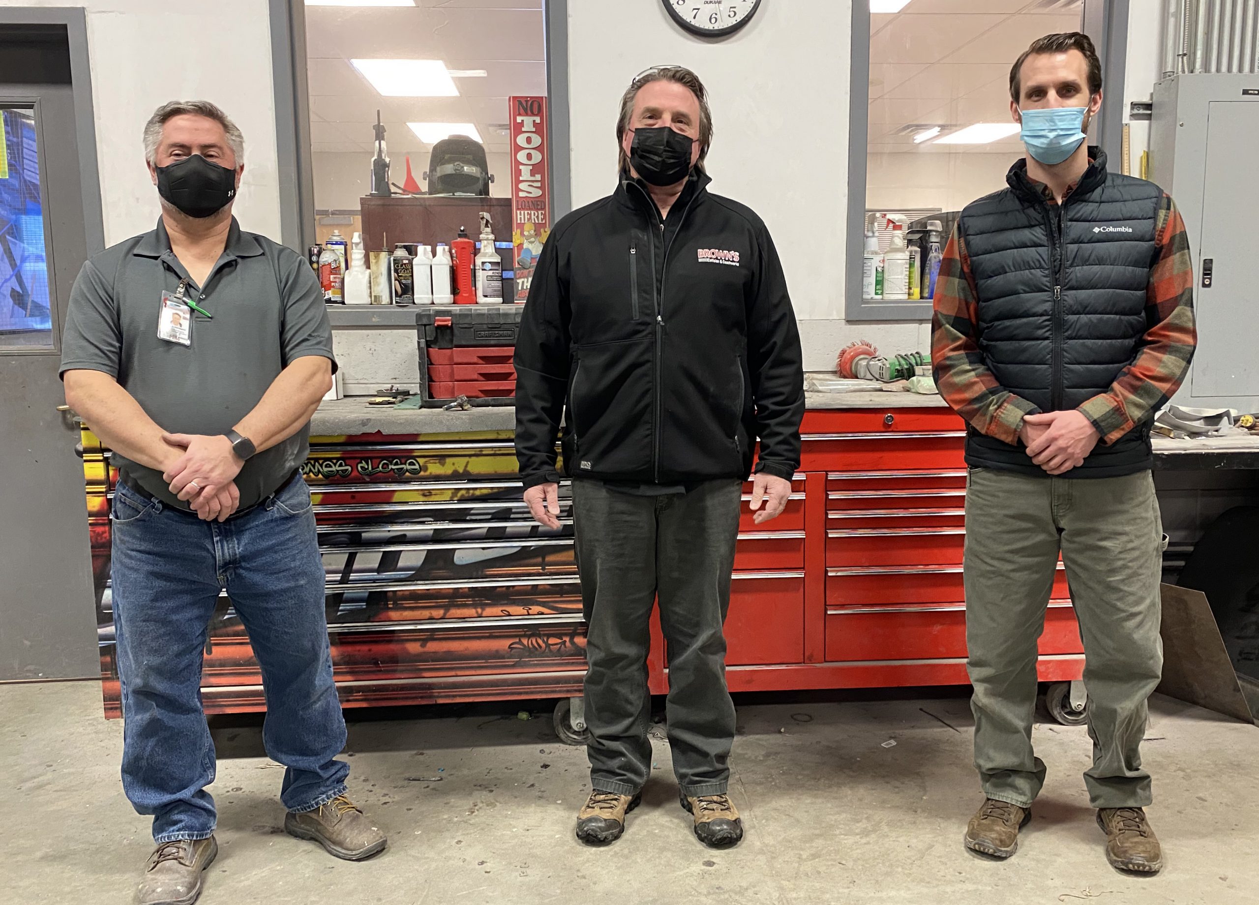 Three people pose for a photo in front of a red tool chest.