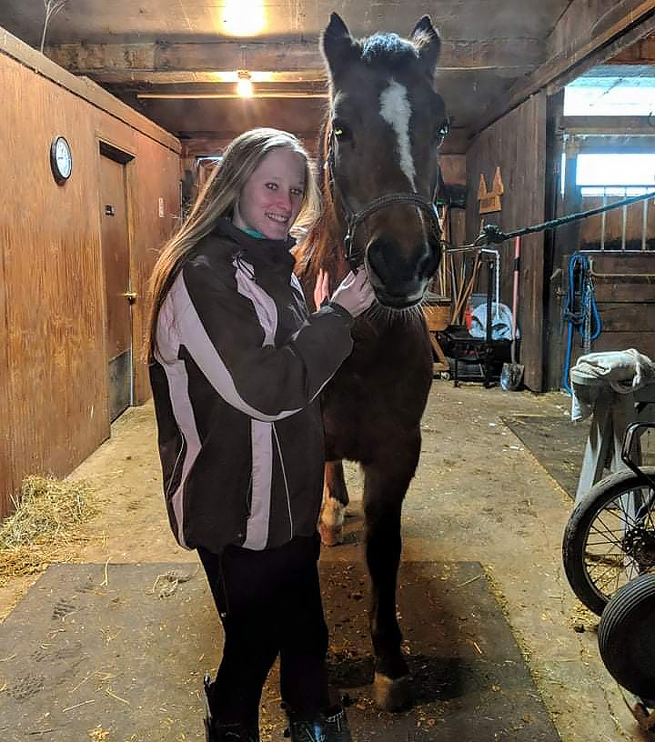 Kelsey stands next to a horse in a barn