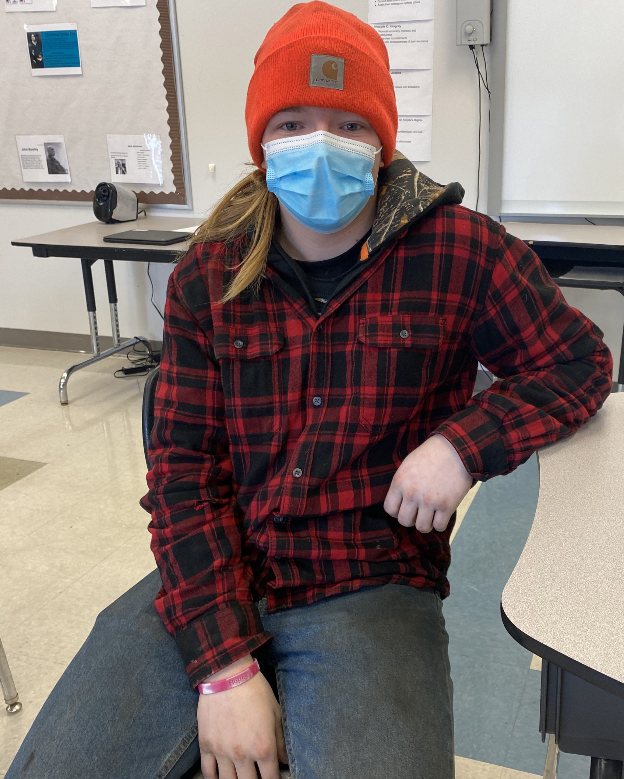 A student poses for a photo sitting in a chair in a classroom.