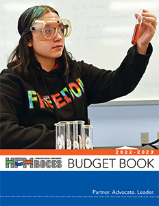 a student holds up a test tube looking at the solution inside while wearing safety glasses. More test tubes are in front of the student.
