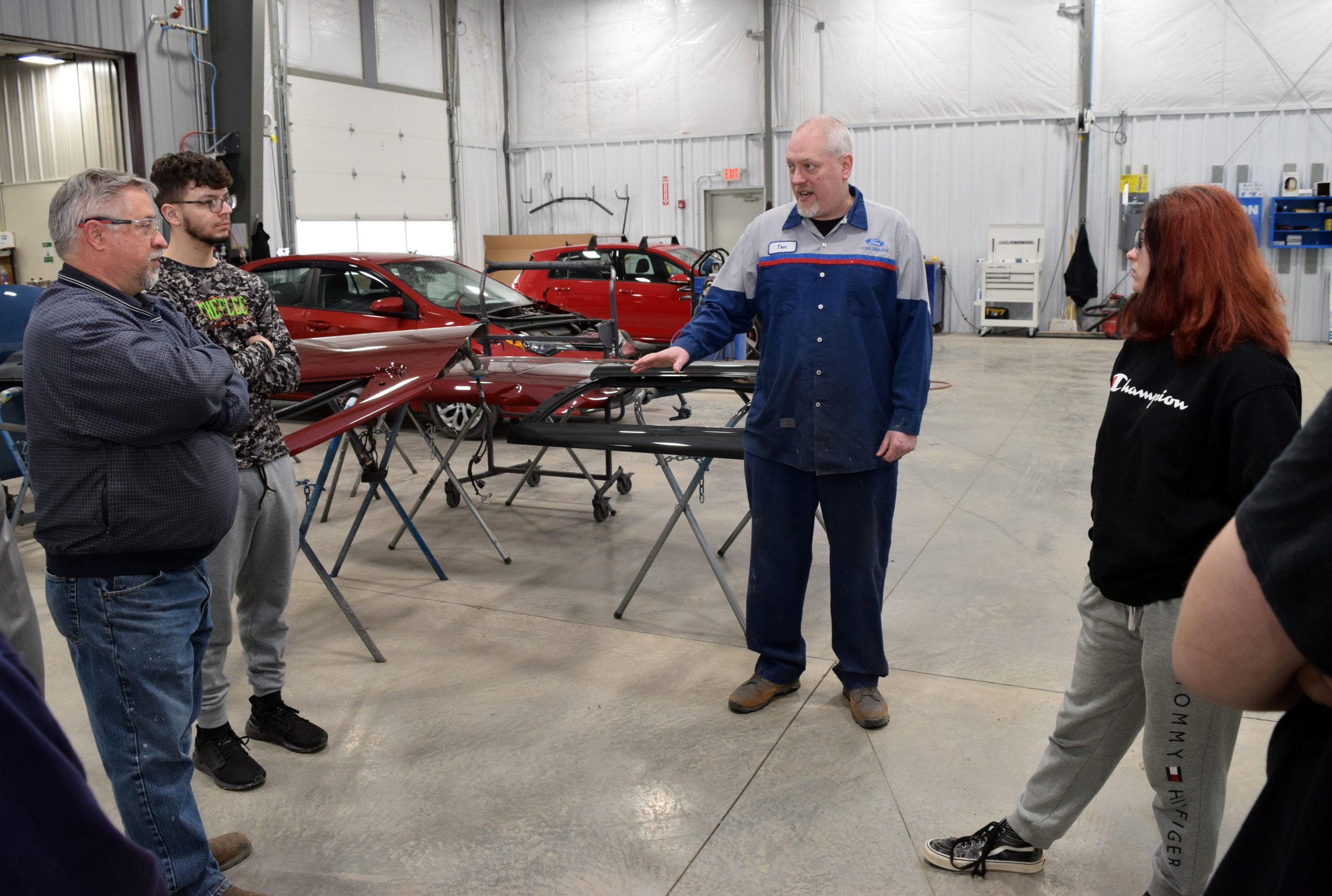 Students stand on the repair floor at Brown's Ford talking with Instructor John Ackermann and Brown's employee Tom Farker