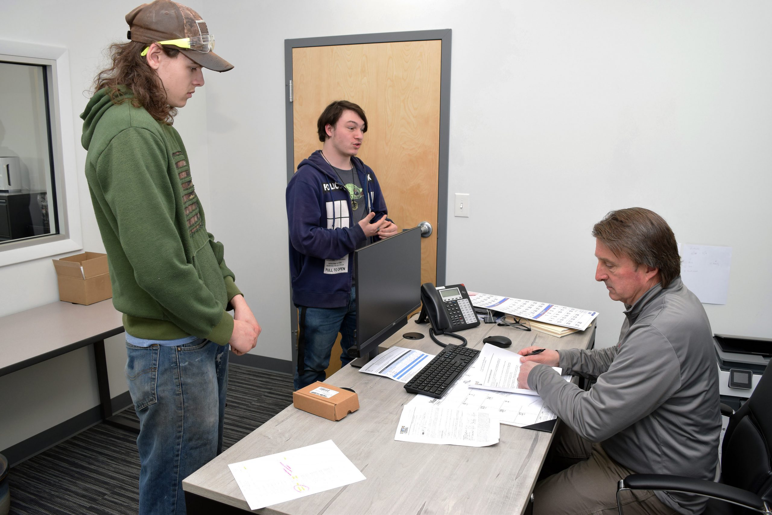 Two student stand in front of Derek Brown as he sits 