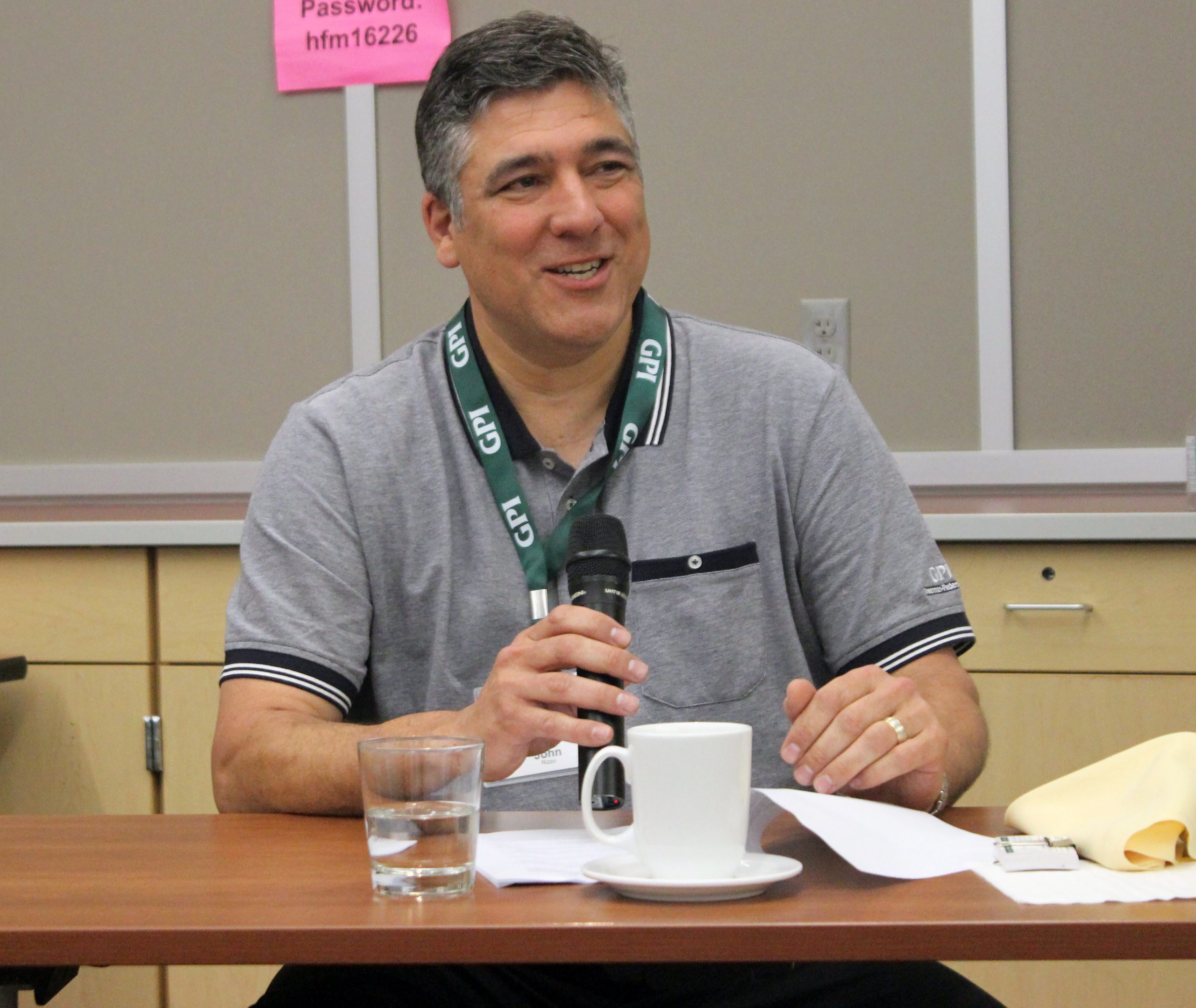 John Rizzo sits at a table and speaks into a microphone