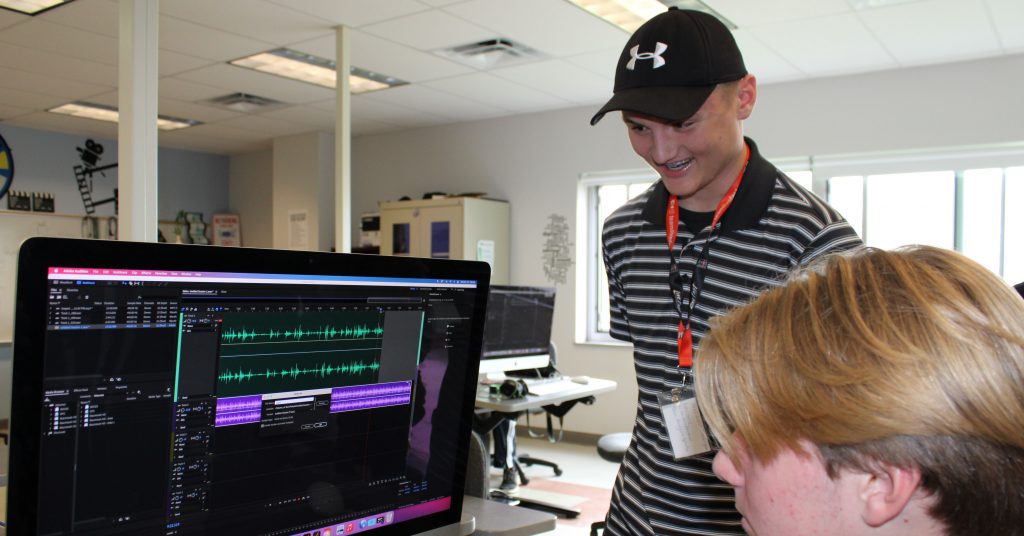 Brady Houser stands at computer next to another student in the Digital Multimedia classroom at HFM BOCES