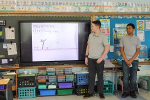 A male PTECH student stands in front of a classroom while discussing his story book written in Mandarin