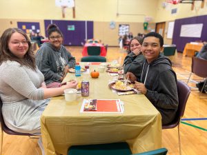 Four PTECH students smile for the camera as they enjoy their Thanksgiving meals together