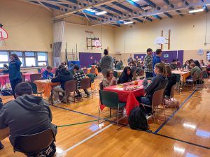 Photo of many PTECH students eating their Thanksgiving meals inside the gymnasium at PTECH at Glebe Street location