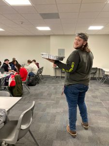 Student standing in a classroom holding a tray smiling at the camera