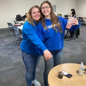 Two female students stand and pose for a picture in a classroom