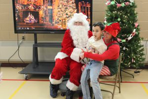 A students sits on a teacher's lap while meeting Santa Claus during his visit to Meco Academy