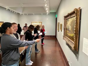 A student points at a painting inside a gallery at the Arkell Museum in Canajoharie, NY while speaking with another classmate.