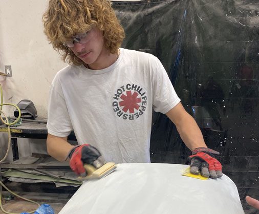 A student sands a car door panel. 